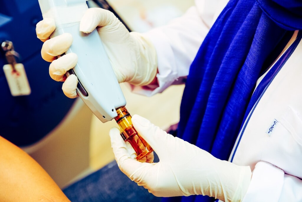Gloved aesthetic practitioner handling a clinical microneedling device with sterile technique in a professional clinic