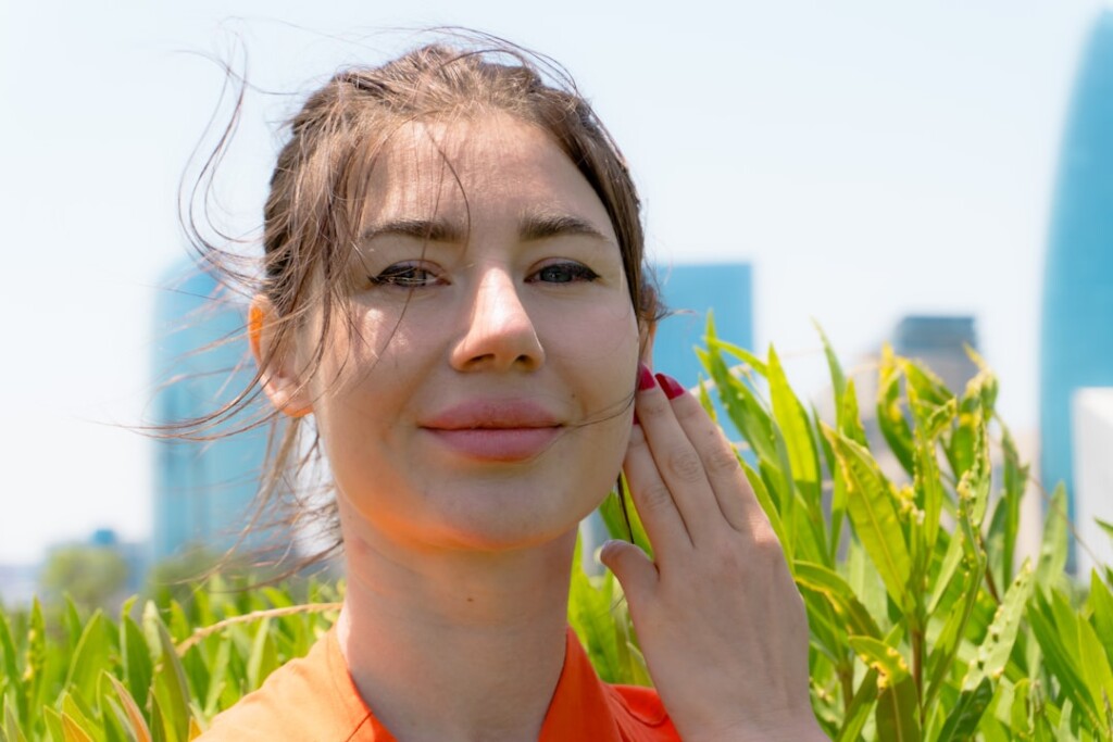 Young woman with healthy glowing skin touching her cheek outdoors in natural light, representing lifestyle factors that affect filler longevity