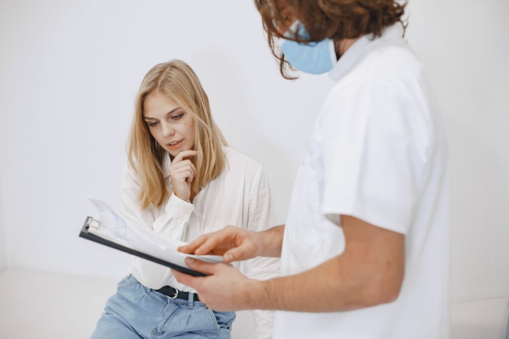A patient thoughtfully reviewing consultation documents with a masked medical professional at a cosmetic clinic