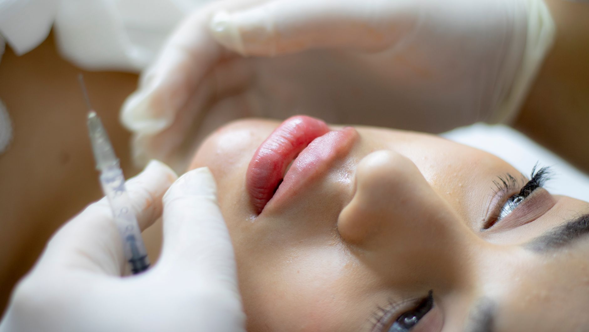 Close-up of a woman receiving a lip augmentation injection from a gloved professional at a beauty clinic